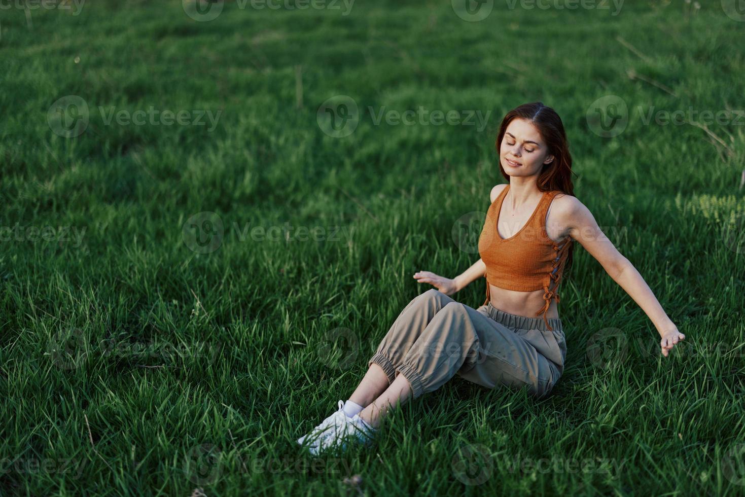 A happy woman looks out at the setting summer sun sitting on the fresh green grass in the park and smiling, view from above. The concept of self-care photo