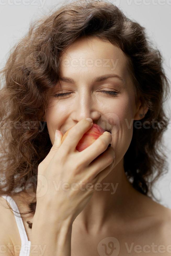 Closeup portrait of happy curly beautiful woman in basic white t-shirt enjoy fresh apple fruit posing isolated on over white background. Natural Eco-friendly products concept. Copy space photo