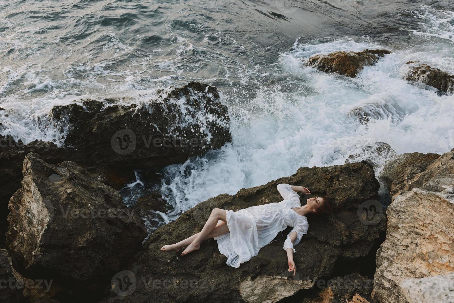 atractivo mujer con largo pelo en un aislado Mancha en un salvaje rocoso costa en un blanco vestir vacaciones concepto foto