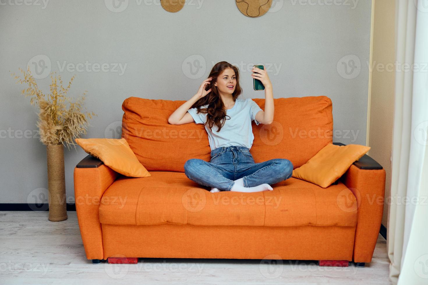 portrait of a woman chatting on the orange couch with a smartphone unaltered photo