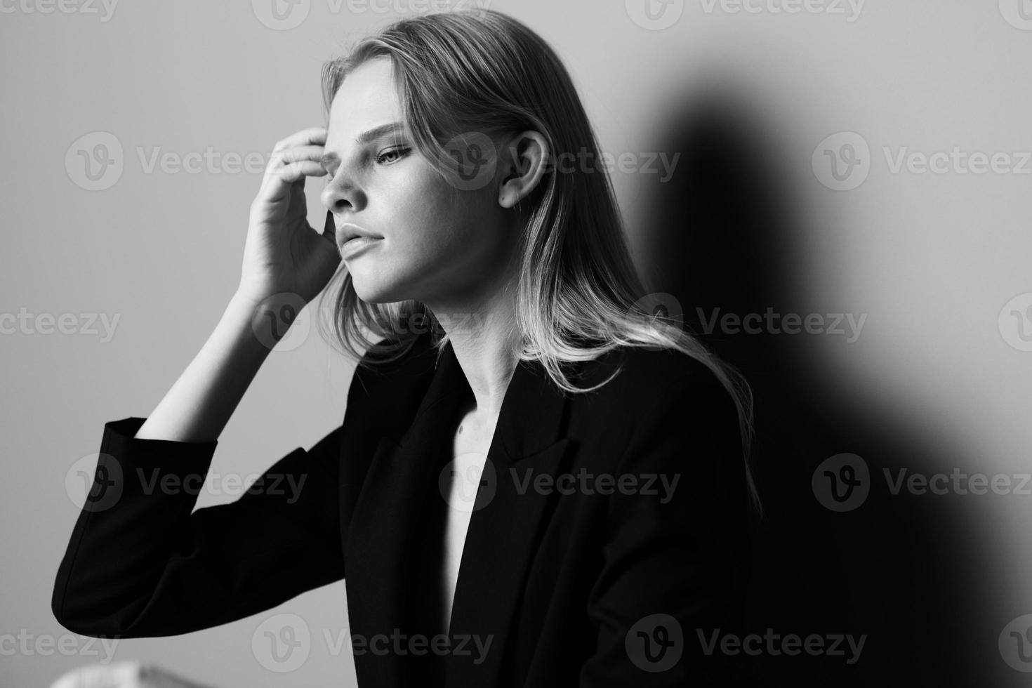 Aesthetic pensive sad blonde young model posing in classic jacket touching stocking hair at studio. Beautiful lady thoughtful looking and caress her curls. Black and White concept photo