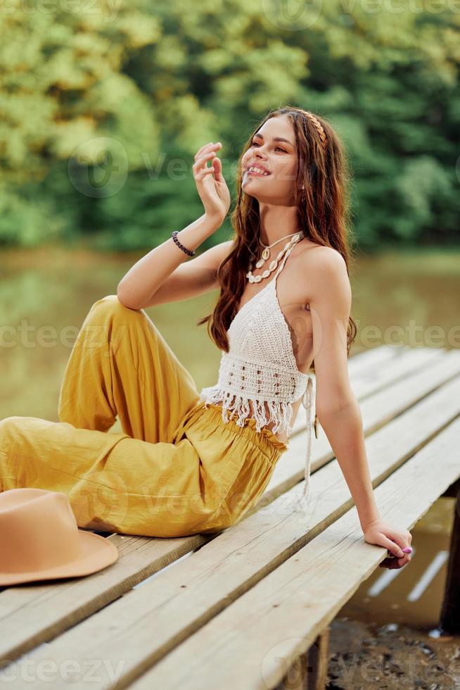 A young hippie woman sits on a lake bridge wearing stylish eco clothes and  smiling 22065127 Stock Photo at Vecteezy