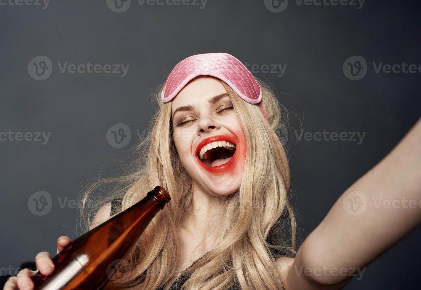 Drunk woman with a bottle of beer having fun on a gray background and gesturing with her hands photo