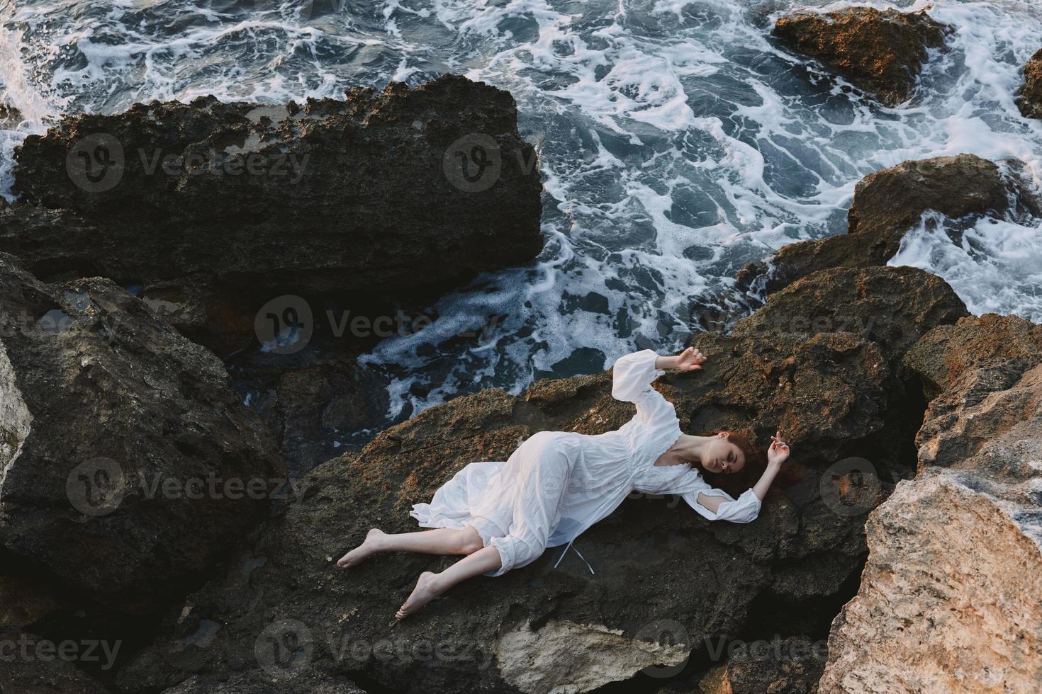 woman in long white dress wet hair lying on a rocky cliff landscape photo