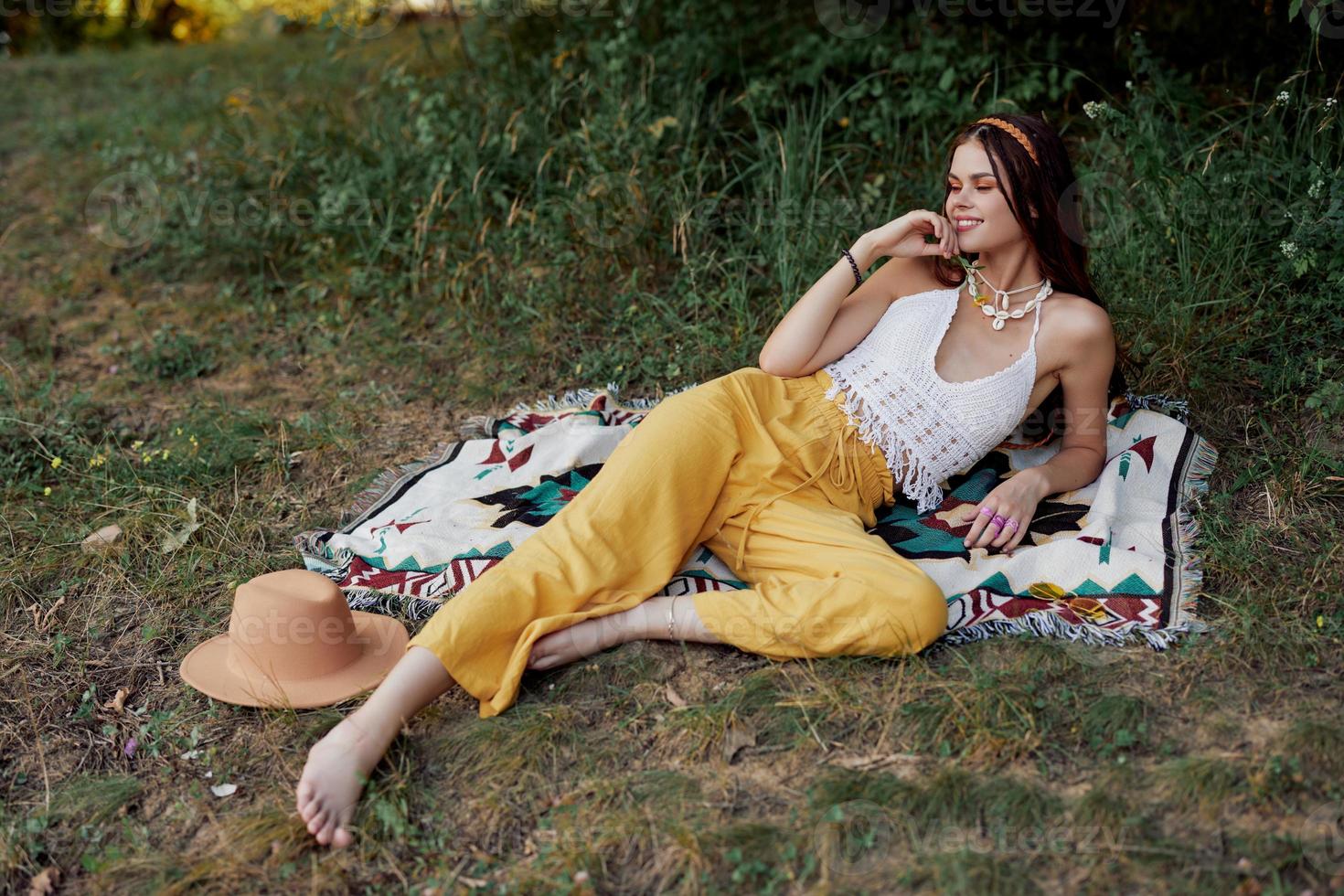 joven hermosa hippie mujer acostado en el suelo en naturaleza en el otoño en eco ropa en amarillo pantalones en el puesta de sol ligero foto