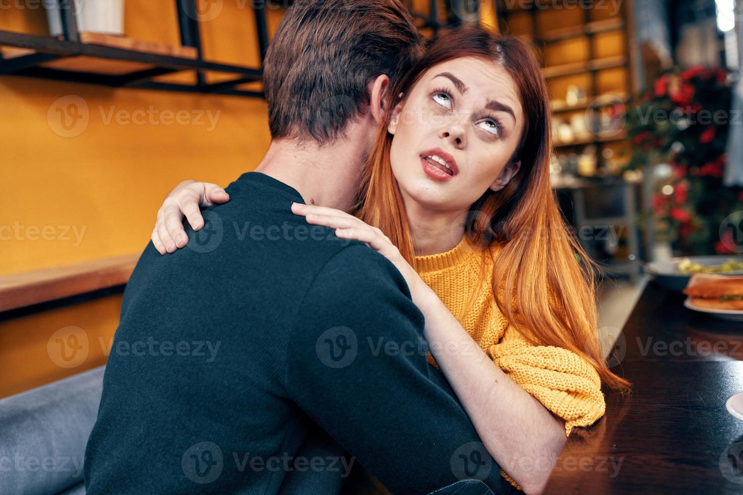 romantic woman hugs a young man in a sweater at a table in a cafe interior a couple in love photo