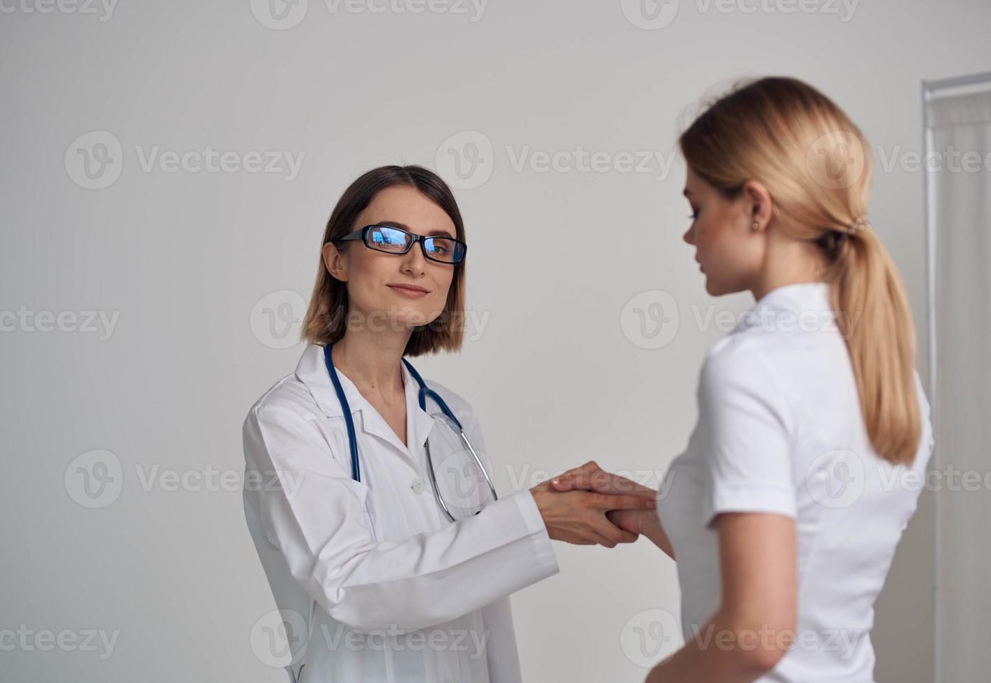 mujer médico en un médico vestido batidos manos con un paciente en un blanco camiseta en un ligero antecedentes foto