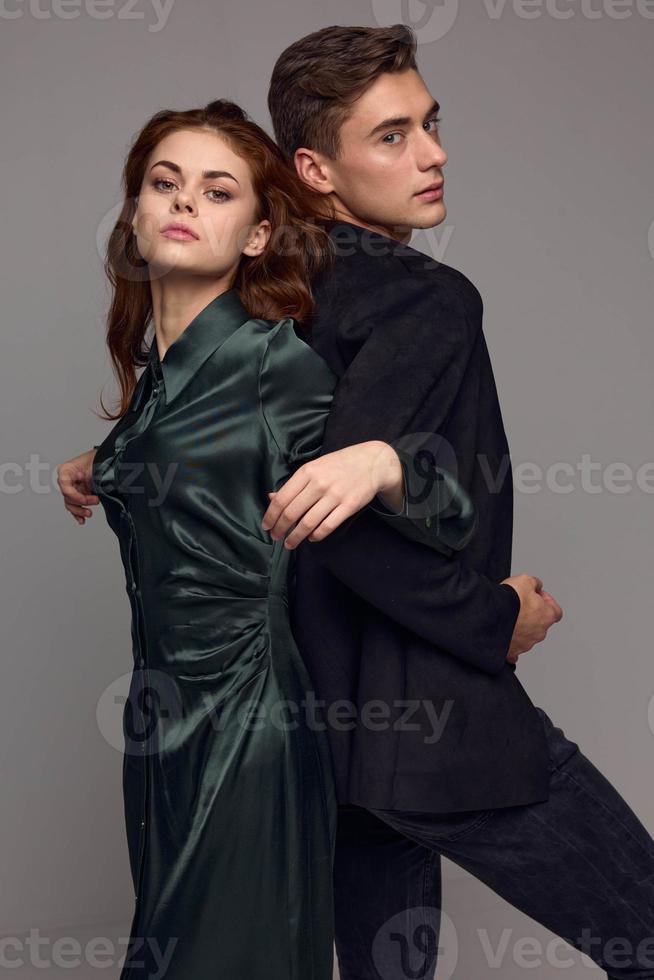 A woman in a dress and a man in a suit stand with their backs to each other with their hands connected photo