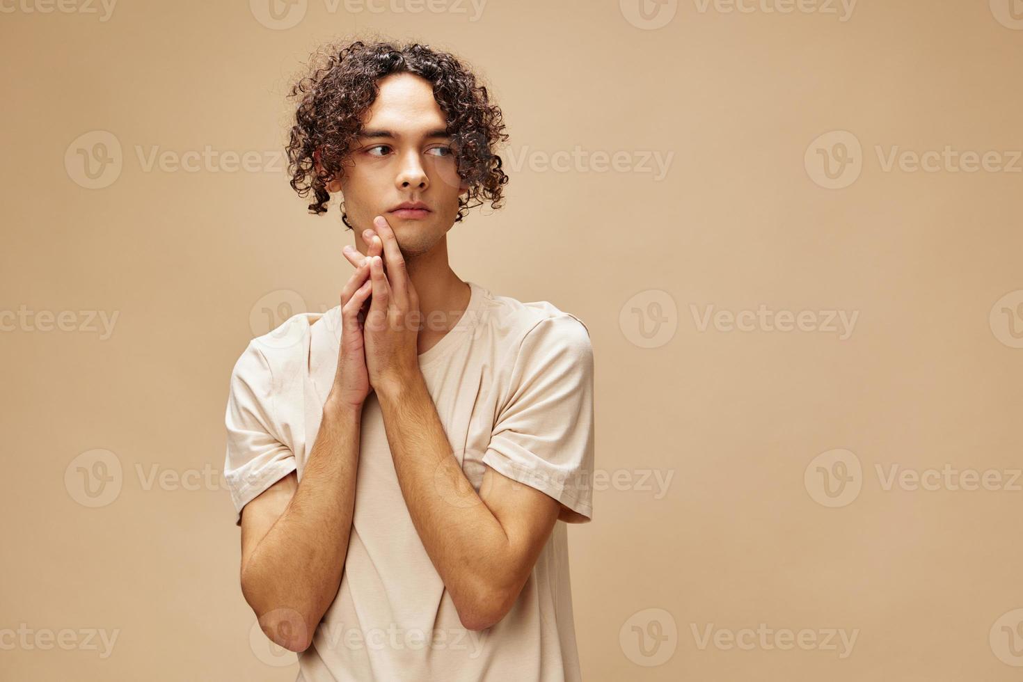 Incredulous shocked awesome tanned curly man in basic t-shirt posing isolated on over beige pastel background. Fashion New Collection offer. People and Emotions concept. Free place for ad photo
