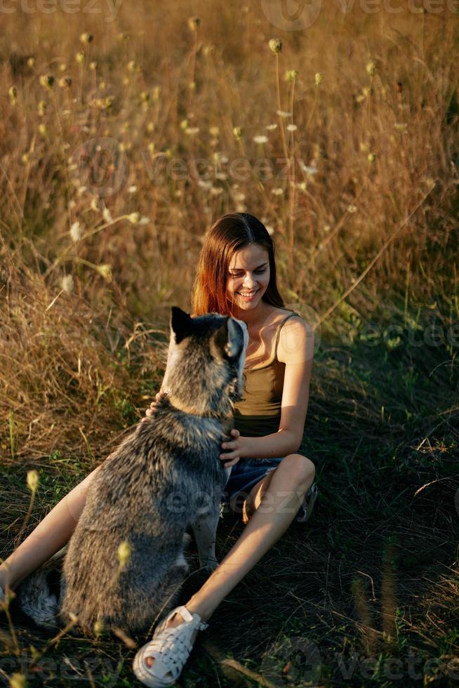 Woman sitting in a field with a dachshund dog smiling while spending time in nature with a friend dog in autumn at sunset photo