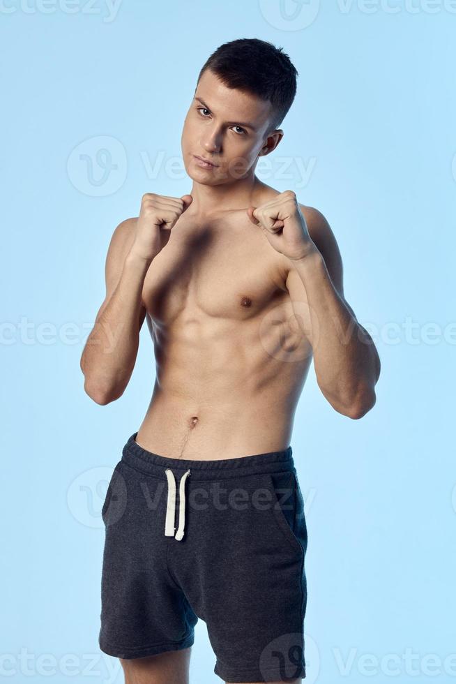 athlete with naked torso gesturing with hands and shorts blue background model cropped view photo