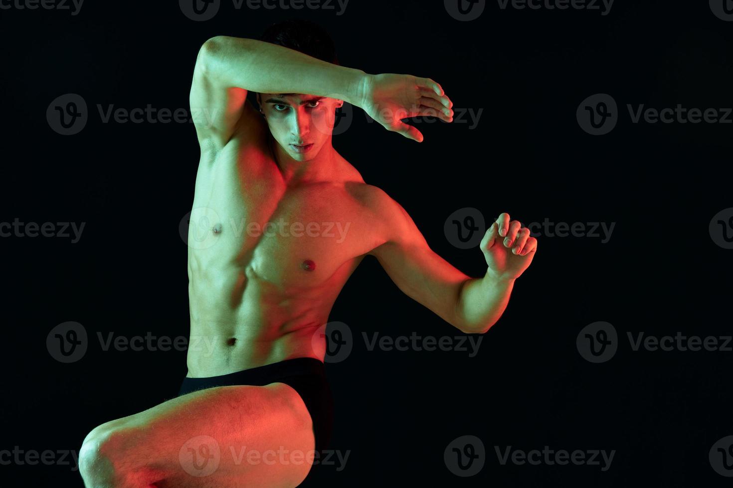 a man athlete with a pumped-up torso raised his leg up on a black background and gestures photo