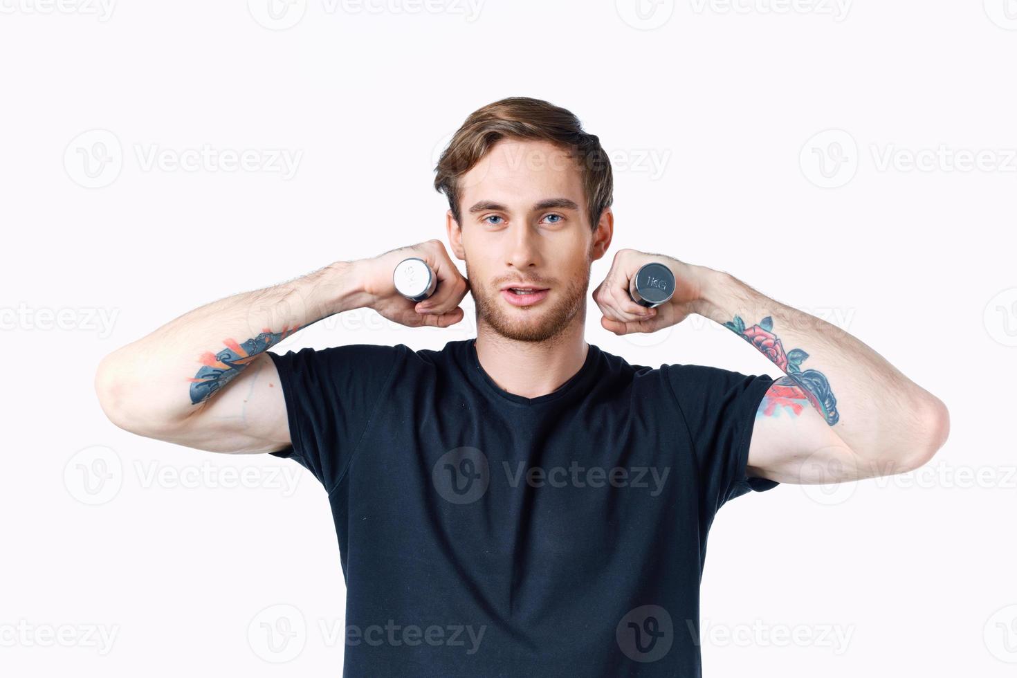 a sporty man in a black t-shirt holds dumbbells near his face on a light background and a black t-shirt photo