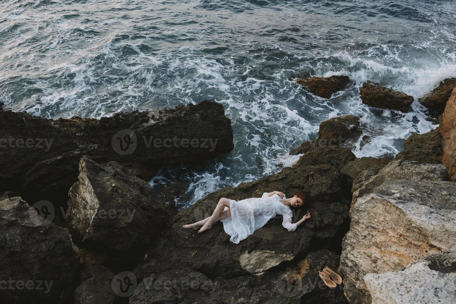 mujer acostado en rocoso costa con grietas en rocoso superficie vacaciones concepto foto