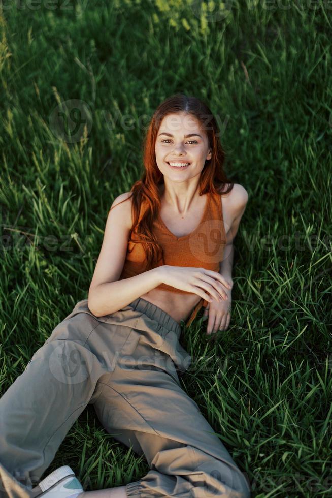 View from above a woman lying on the grass smiling and looking into the cameras happy lifestyle in the park on the green grass in the sunset light photo
