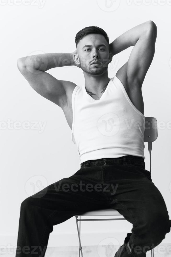 Modelling snapshots. Serious self-confident attractive handsome muscular guy man raise hands up sitting on chair in white studio background. Black and White concept. Copy space photo