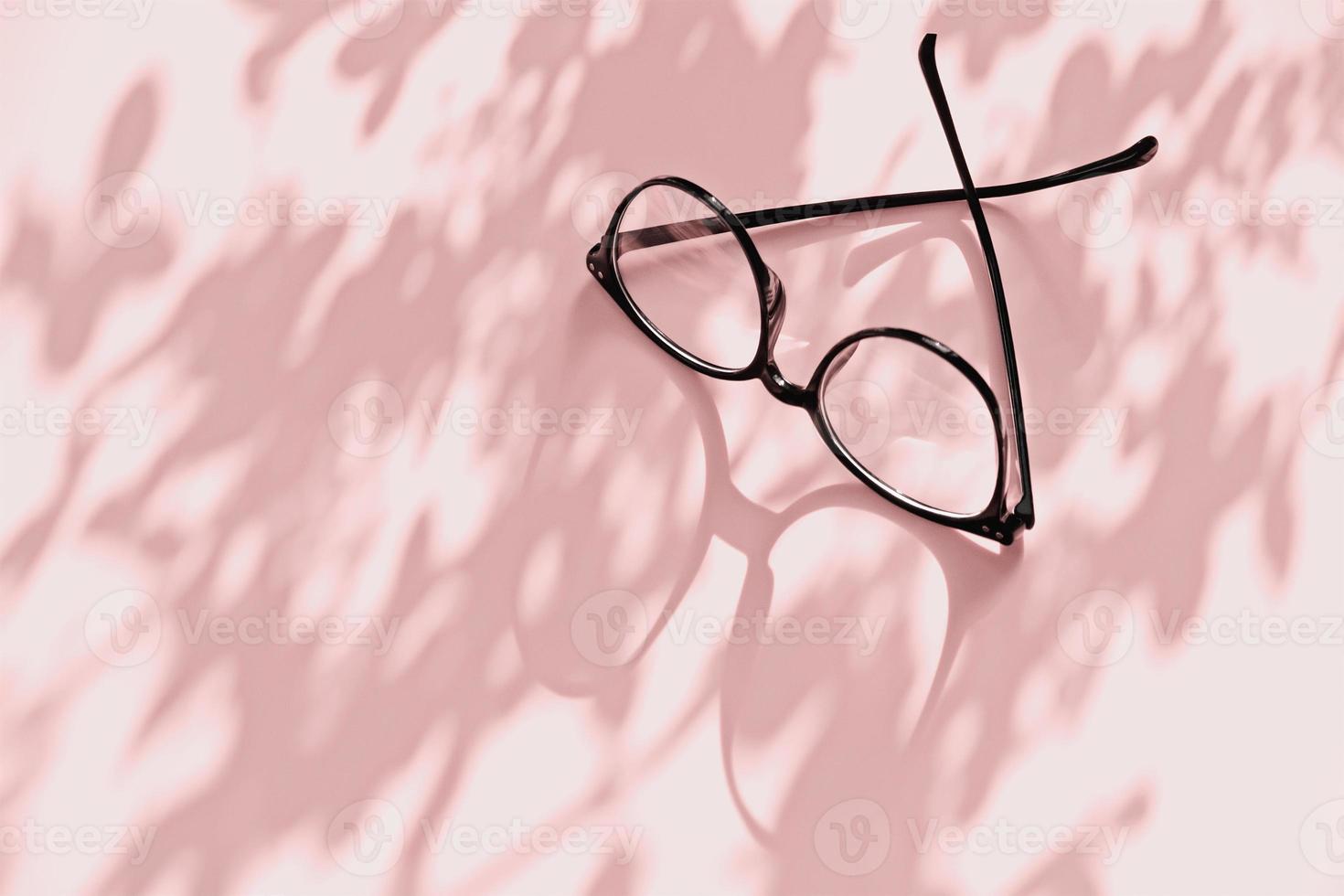 Eyeglasses on pink background with flower shadows and copy space photo