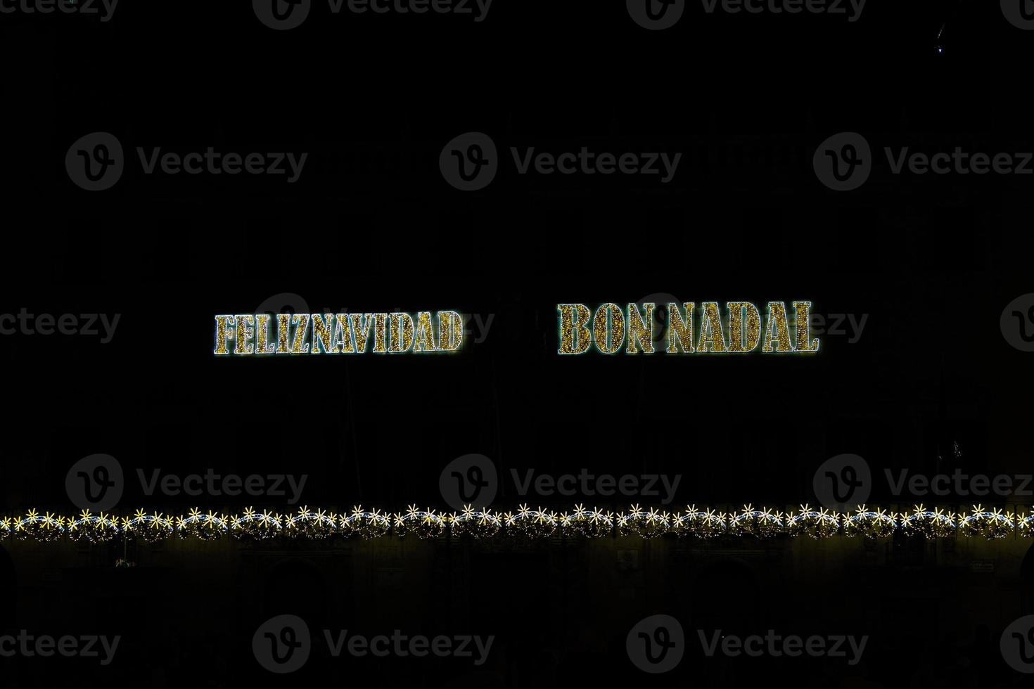 golden shiny neon inscription merry christmas on a black background in Spanish and Catalan, Valencian photo