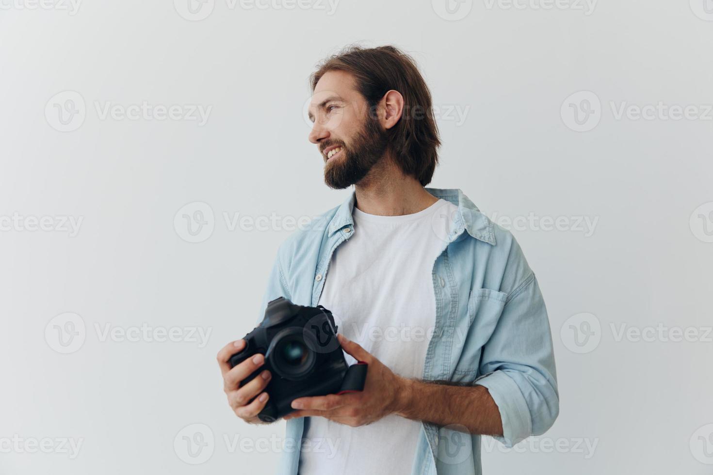 Man hipster photographer in a studio against a white background holding a professional camera and setting it up before shooting. Lifestyle work as a freelance photographer photo