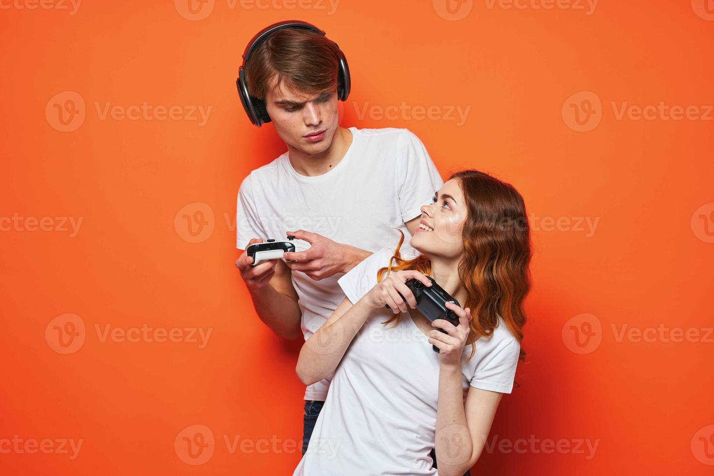 young couple in white t-shirts with joysticks in hands playing game friendship orange background photo