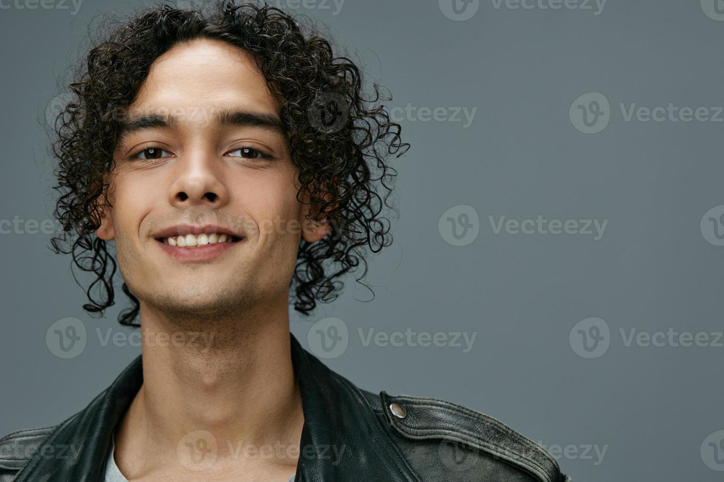 Close up portrait of attractive stylish tanned curly man leather jacket posing isolated on over gray studio background. Cool fashion offer. Huge Seasonal Sale New Collection concept. Copy space for ad photo