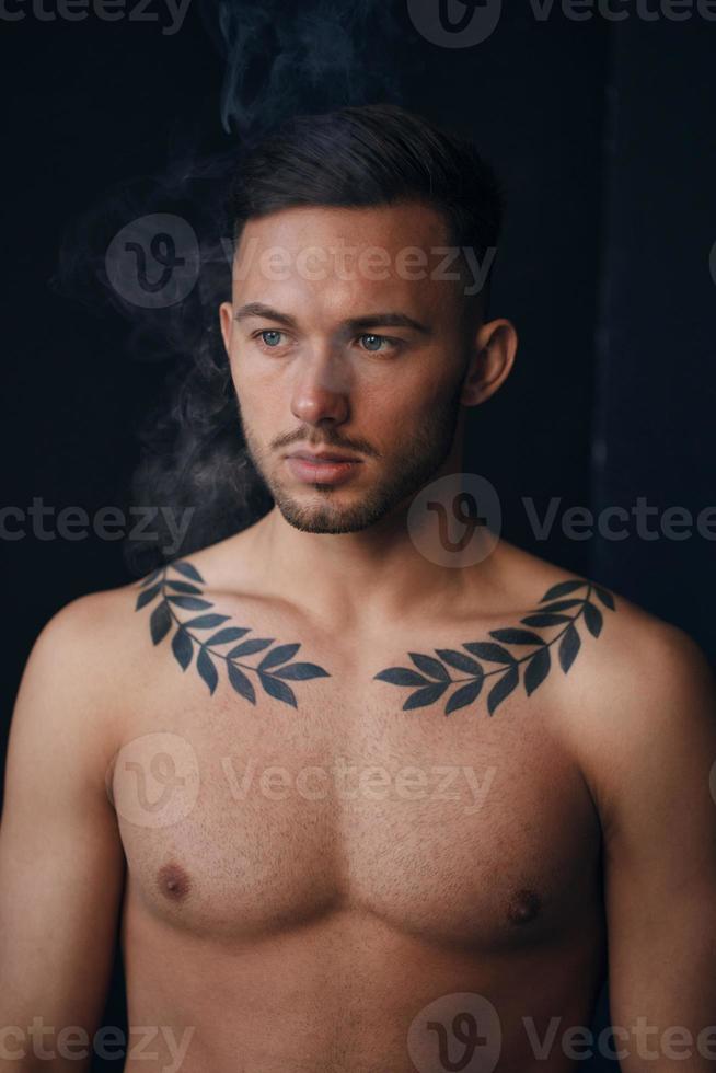 Modelling snapshots. Pensive serious tanned attractive handsome naked man thinking looks aside smoking posing isolated in black studio background. Fashion offer. Copy space for ad. Closeup photo