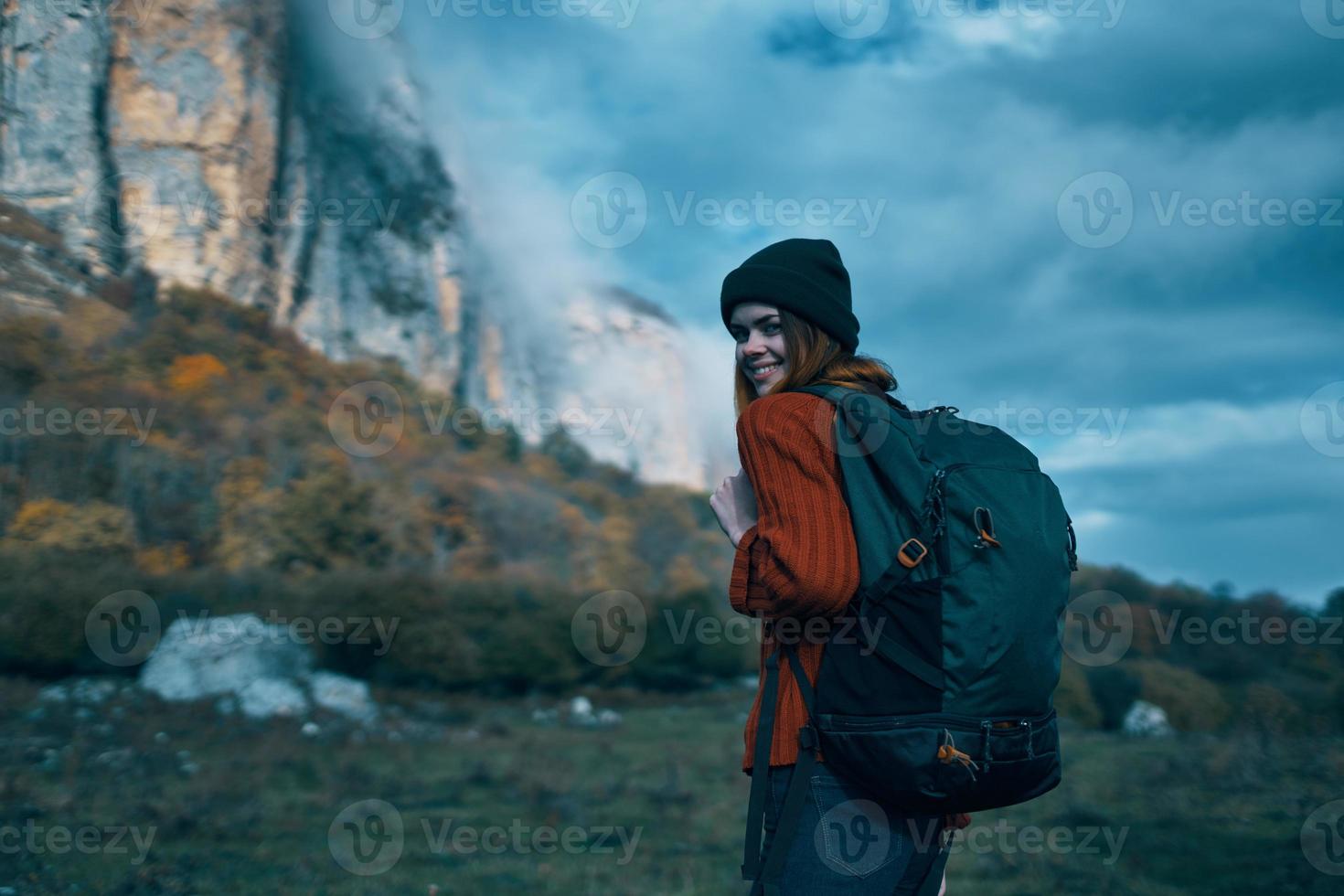 woman traveler in a sweater with a backpack on her back in autumn in the mountains on nature and sky clouds photo