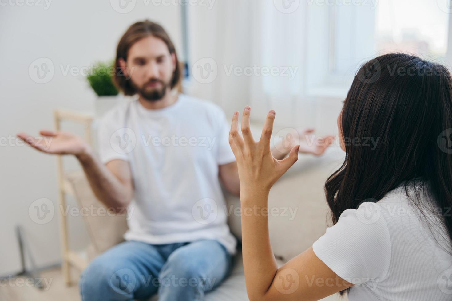 un hombre y un mujer sentar en el sofá a hogar en blanco camisetas y chateando escandalosamente hacer no entender cada otro. un pelea en el familia de dos esposos y agresión foto