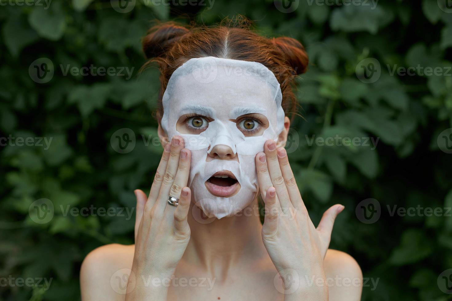 hermosa mujer anti-envejecimiento máscara sorprendido a toque tu cara con tu manos desnudo espalda arbustos en el antecedentes foto