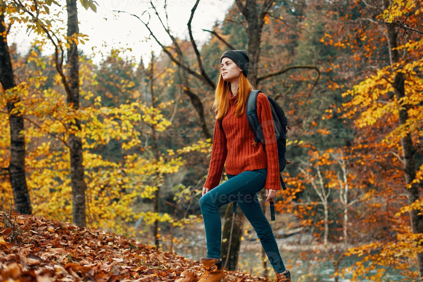 happy woman hiker with a backpack on her back in jeans and a red sweater in the autumn forest park landscape photo