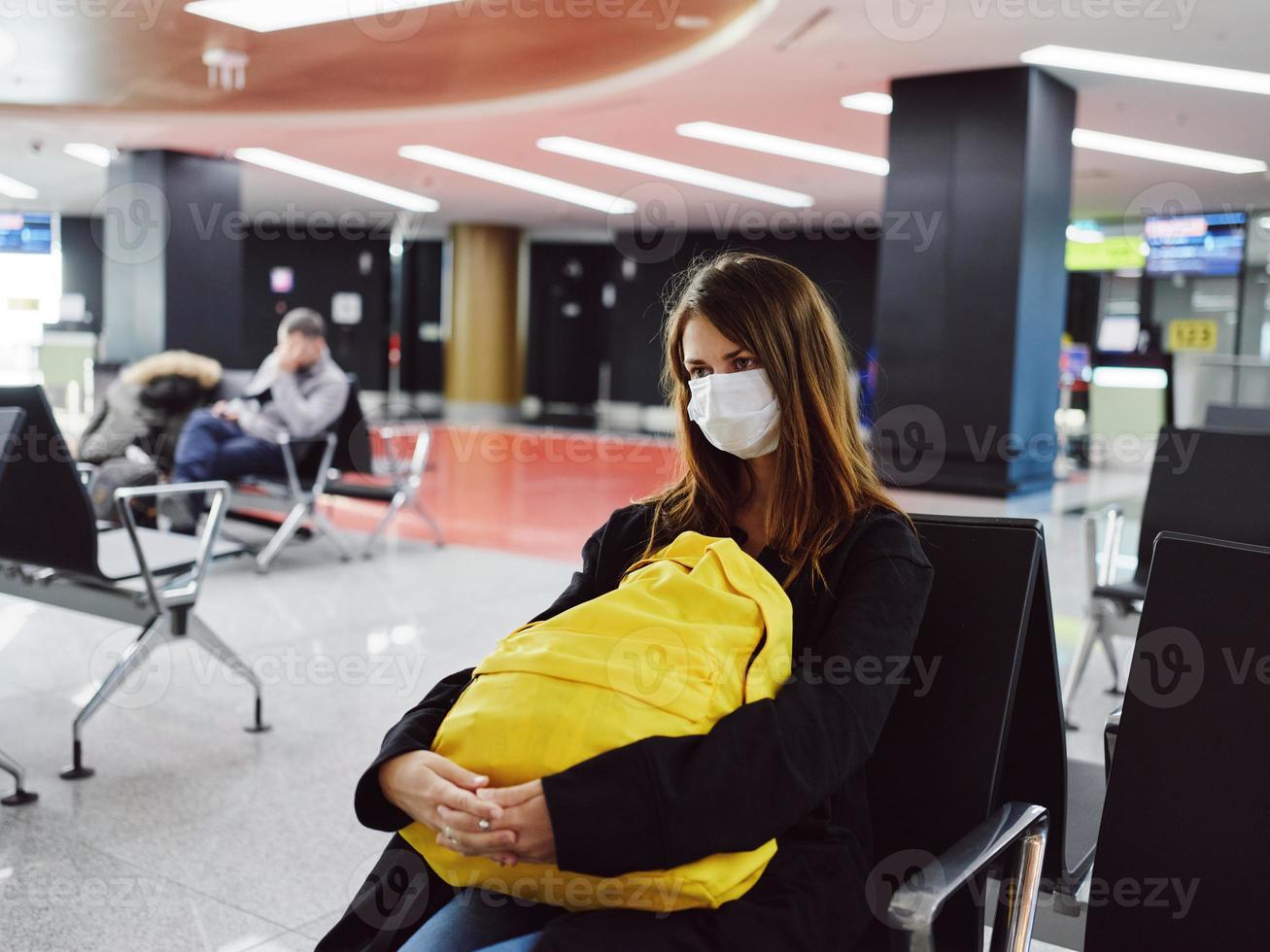 mujer en médico máscara aeropuerto amarillo mochila esperando para vuelo pasajero foto