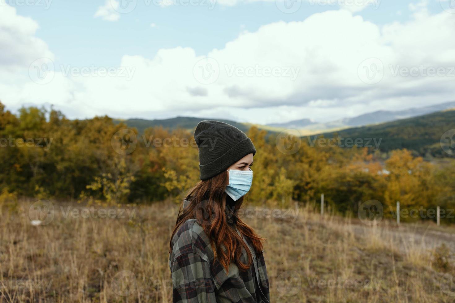 mujer caminante en calentar gorra con un médico máscara en su cara en el bosque foto