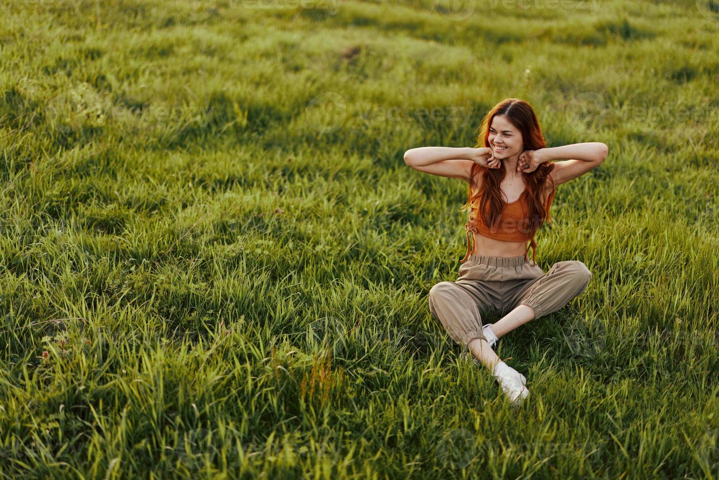 The happy woman smiles and looks out at the setting sun. Long red hair flies in the wind, resting after a walk in the park on the grass photo