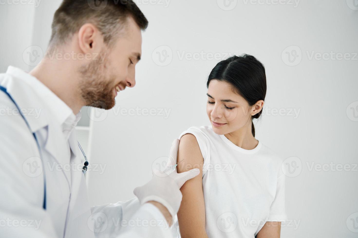 doctor with a stethoscope makes an injection into the shoulder of a woman patient covid vaccination photo