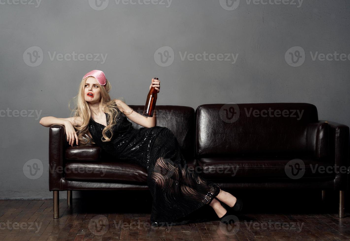 Beautiful blonde woman on the couch with a bottle of beer and in a black dress photo