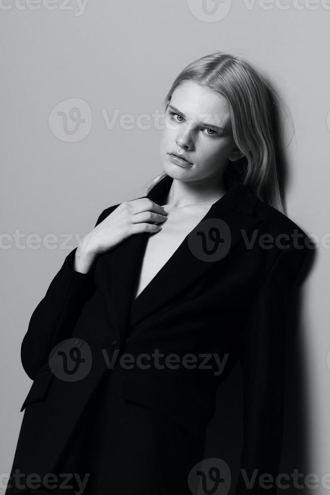 Portrait of a beautiful blonde in a classic jacket leaning against the wall in the studio. Black and white style. Concept for clothing brands photo