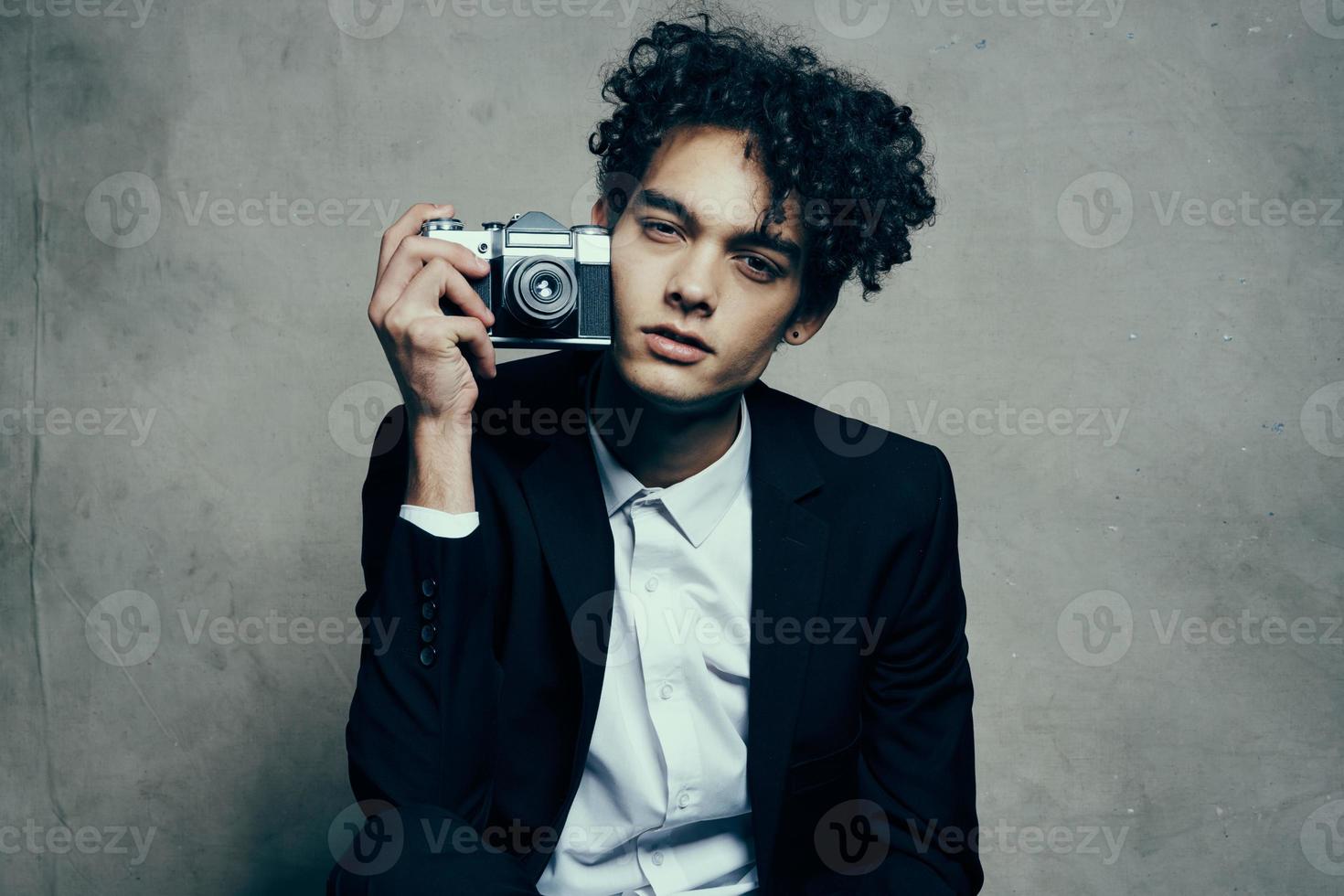 curly-haired man in a jacket and shirt holding a camera in his hand model vogue style photo