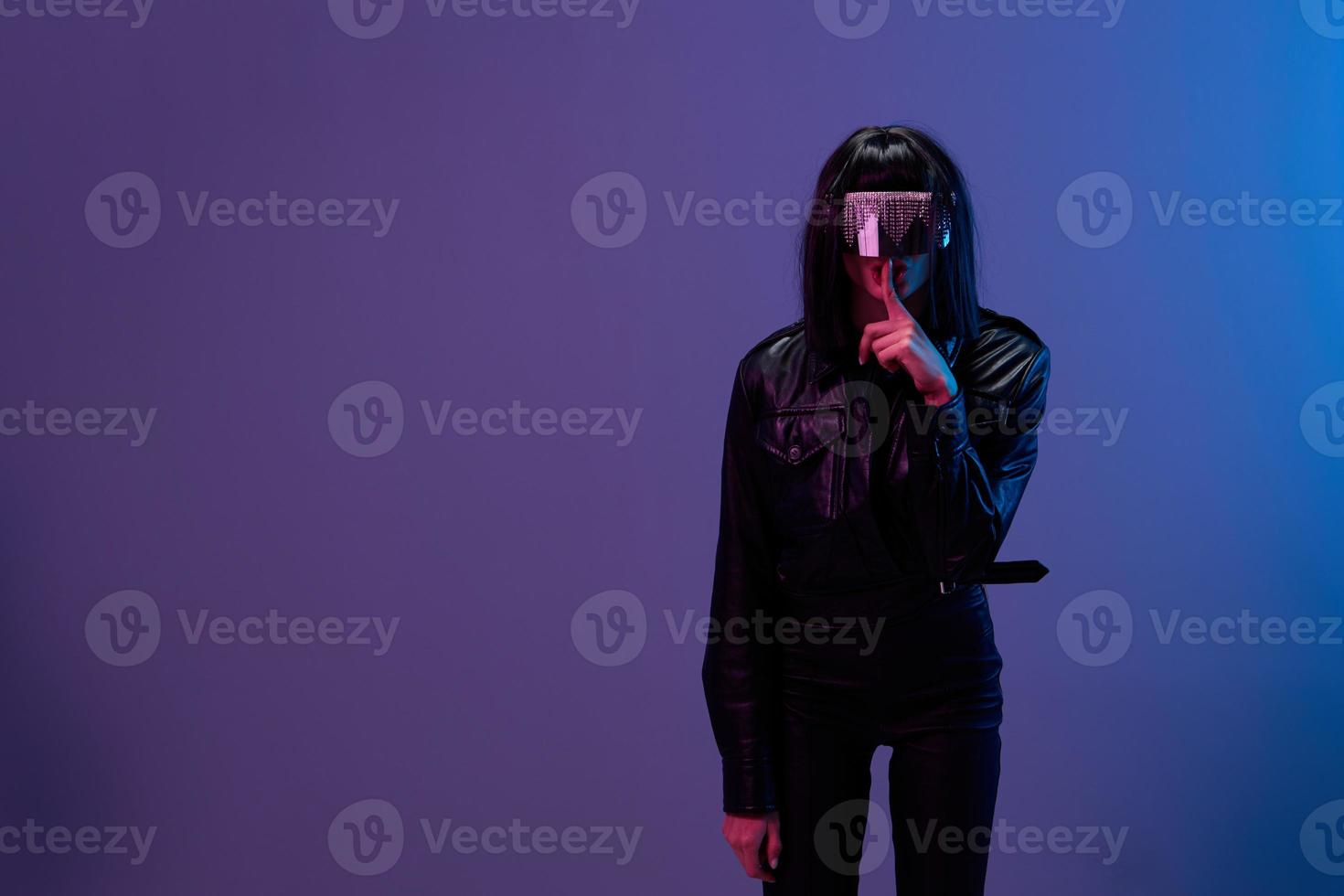 Cool offer. Awesome brunet woman in leather jacket trendy specular sunglasses finger near mouth Shh posing isolated in blue violet color light background. Neon party Cyberpunk concept. Copy space photo