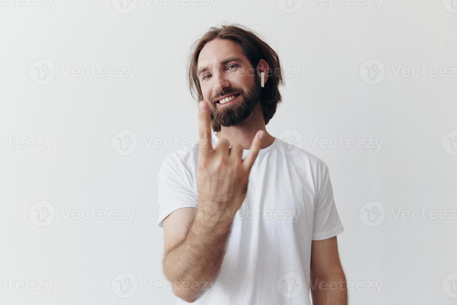 elegante hombre en un blanco camiseta con inalámbrico auriculares en su orejas teniendo divertido escuchando a música sonrisa en un blanco antecedentes estilo de vida foto