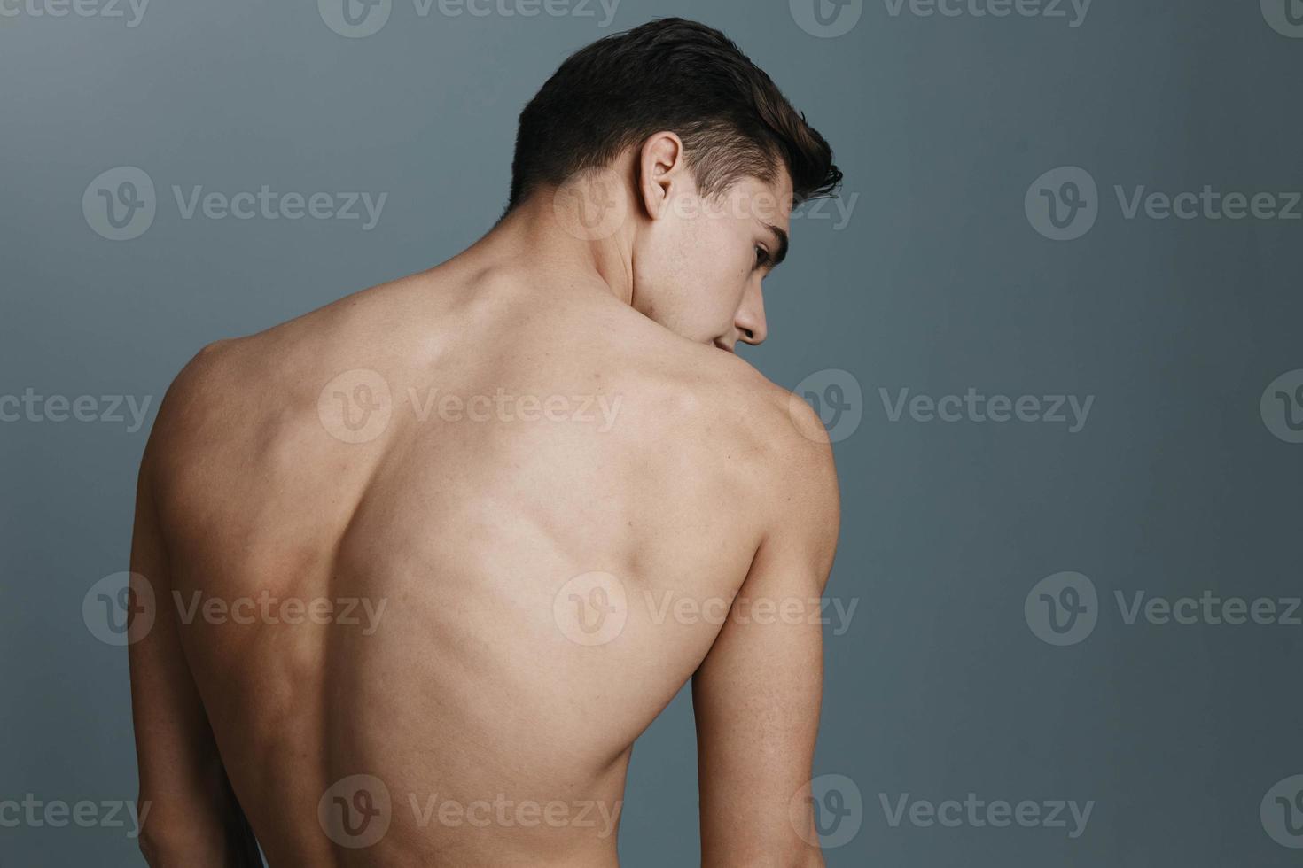 sexy hombre con un desnudo espalda mira a el lado en contra un gris antecedentes foto