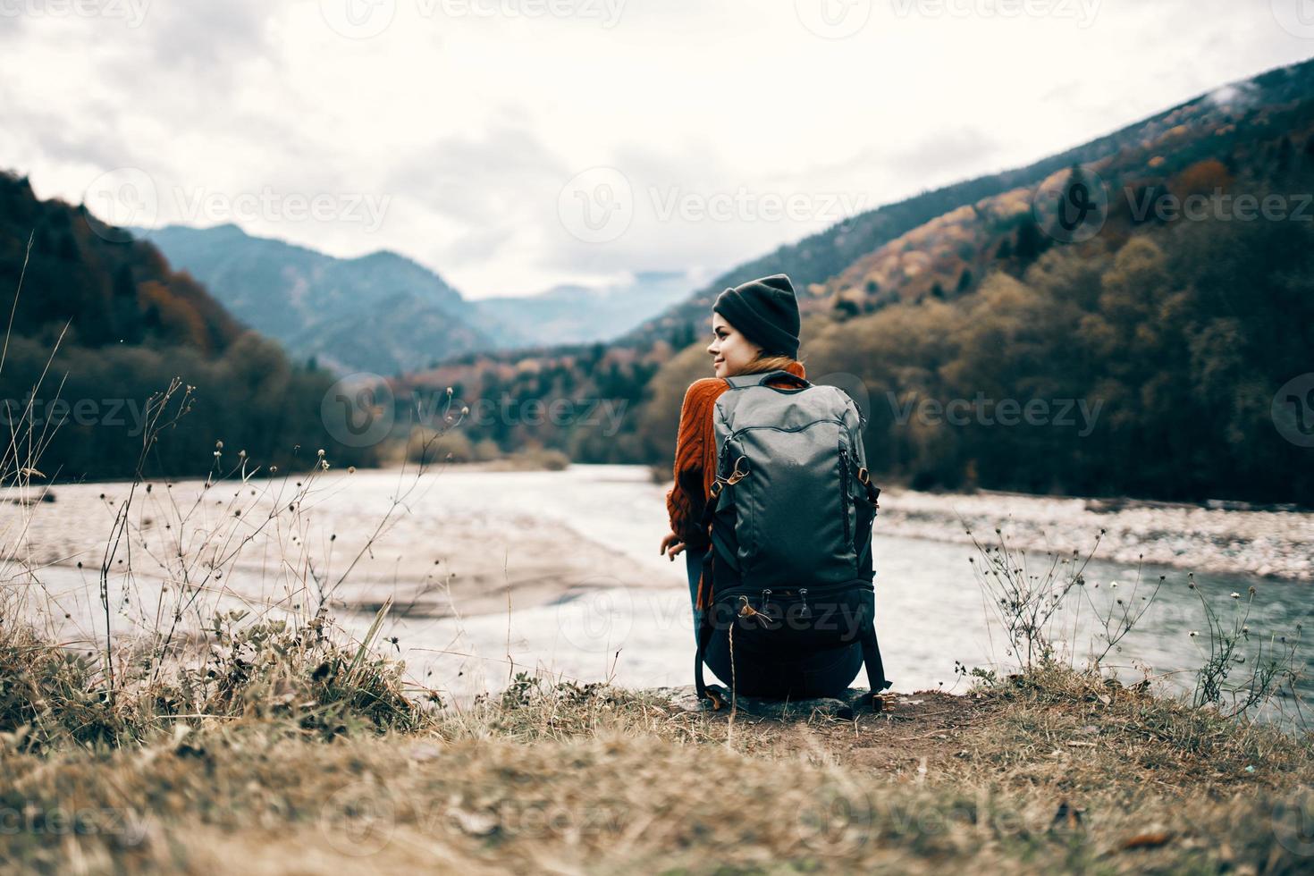 woman traveler with a backpack on her back gestures with her hands and looks at the mountains in the distance photo