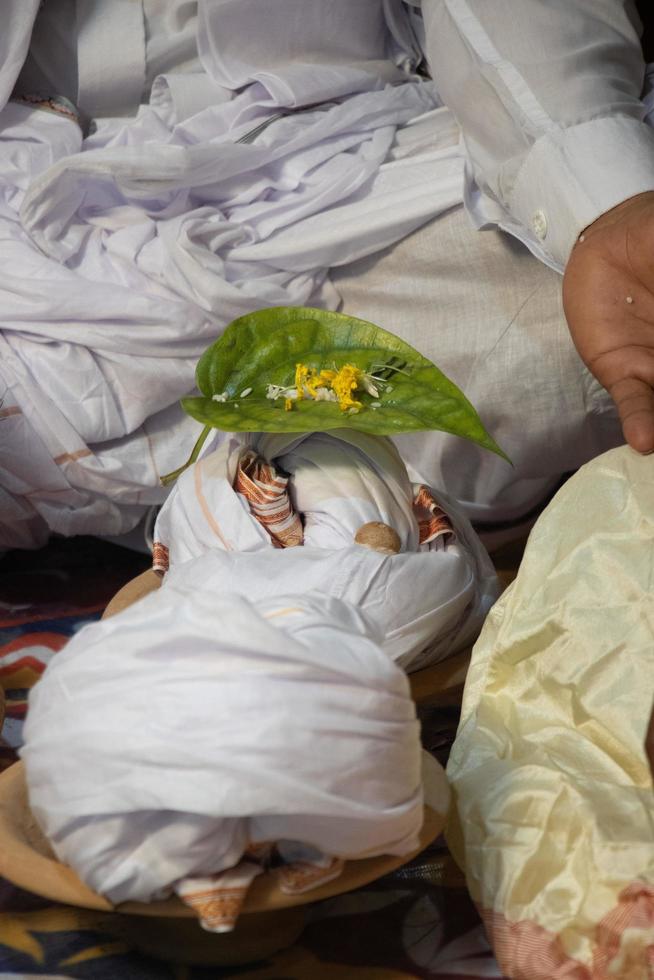 Hindu worship and ritual elements close-up photo. Hindu wedding decoration with white fabric and a betel leaf. Groom sitting in front of some Hindu Puja elements. Traditional Hinduism wedding concept. photo
