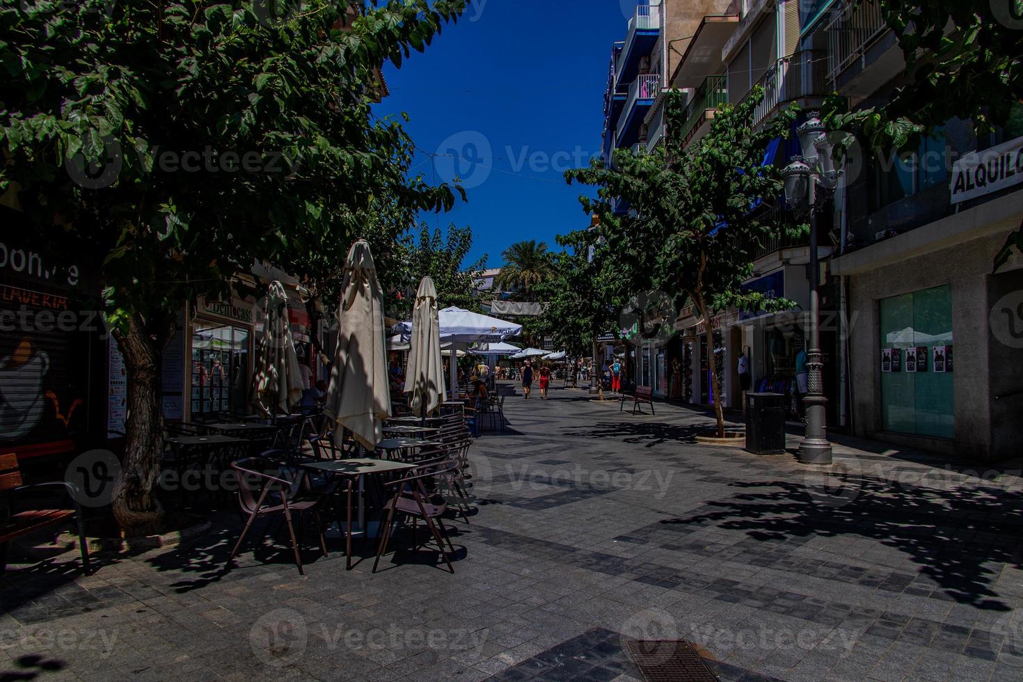 l urbano paisaje de un Español calle en benidorm con un café y mesas en el acera sin personas foto