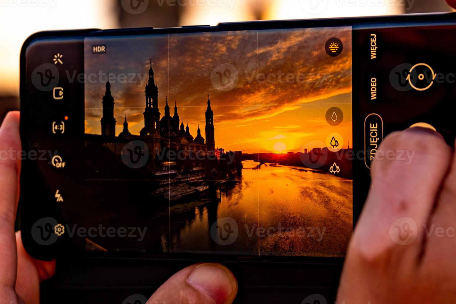 pintoresco puesta de sol en un verano día en el ciudad de zaragoza en España con un ver de el río y el catedral mientras tomando un foto con un móvil teléfono