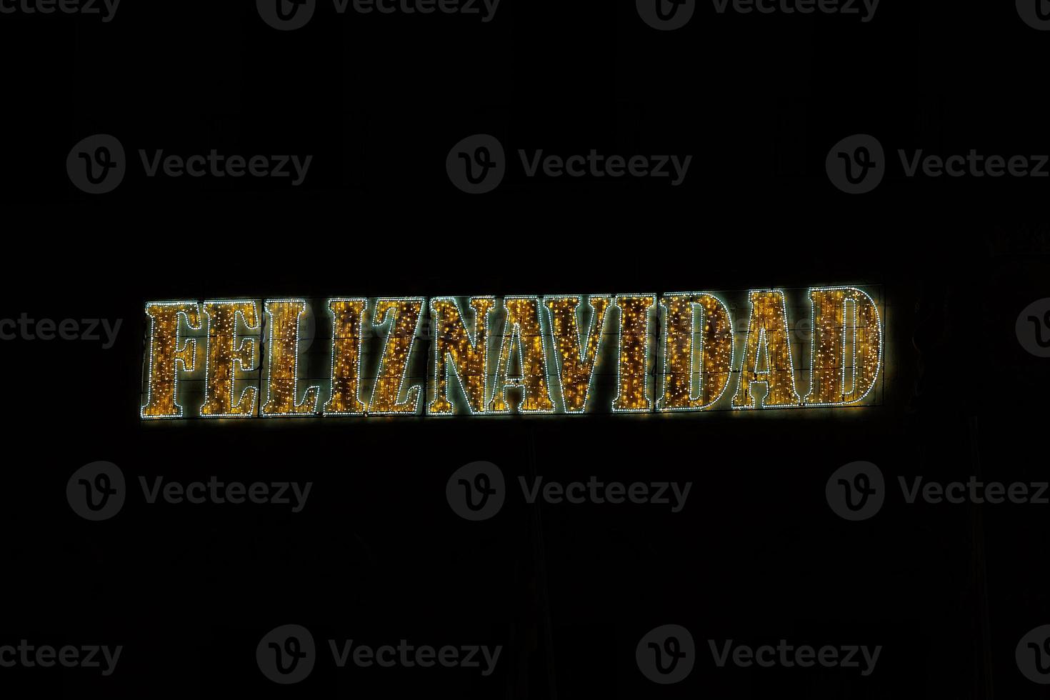 golden shiny neon inscription merry christmas on a black background in Spanish photo