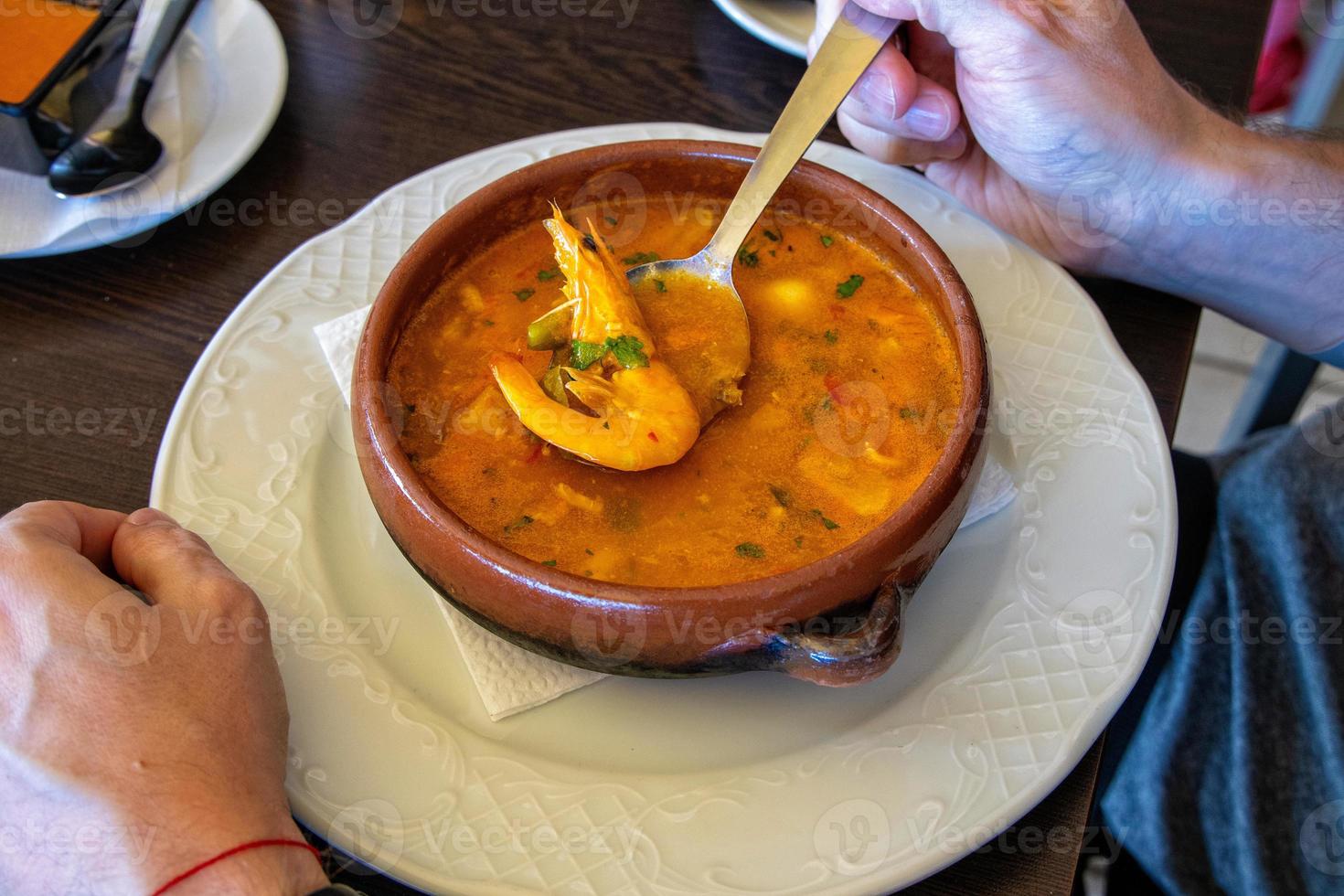 grande arcilla maceta con pescado sopa y camarón mantenido en un cuchara foto