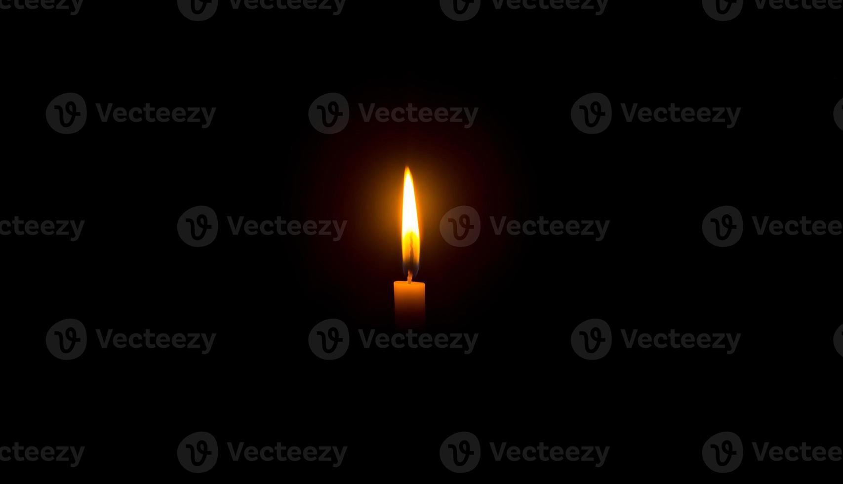 A single burning candle flame or light glowing on an orange candle on black or dark background on table in church for Christmas, funeral or memorial service with copy space photo