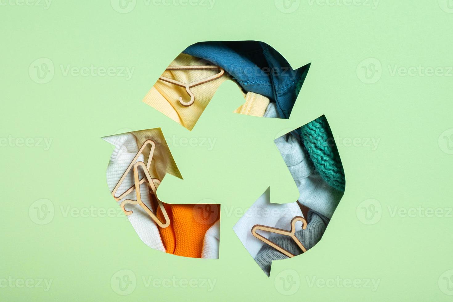 Colorful clothes and mini hungers under paper cut recycling symbol. Second hand, circular fashion and recycling concept photo