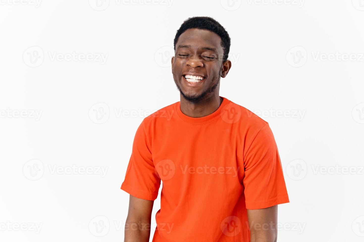 african american guy in an orange t-shirt on a light background laughs photo