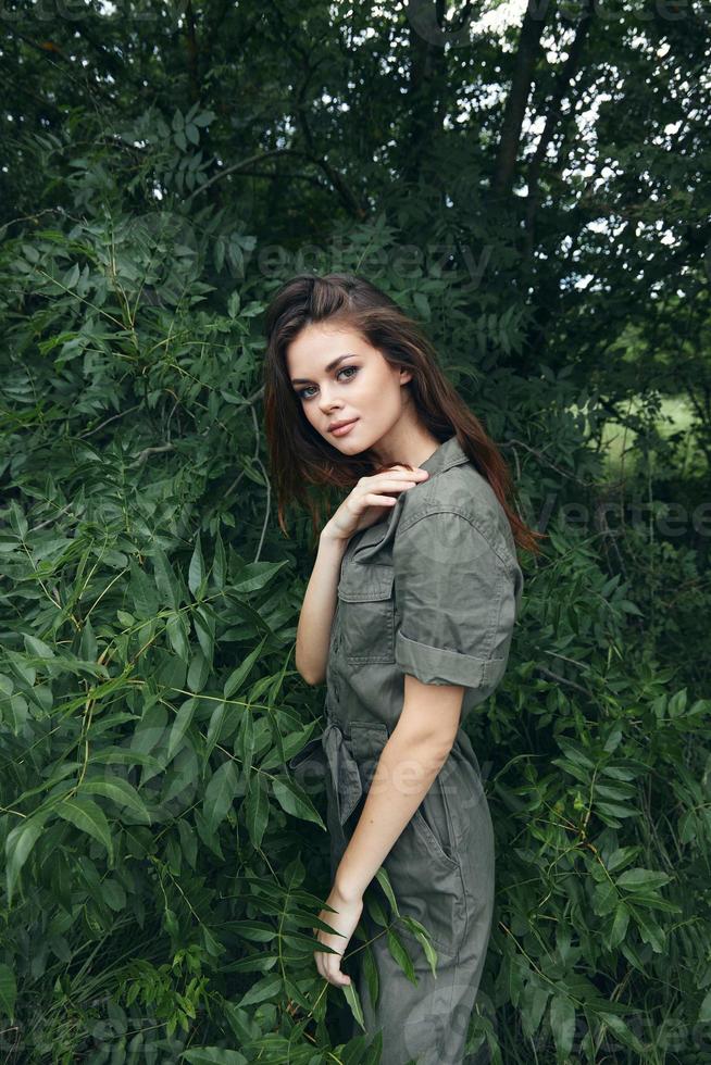 Woman touches shoulder with his hand and a green jumpsuit outdoors green leaves photo